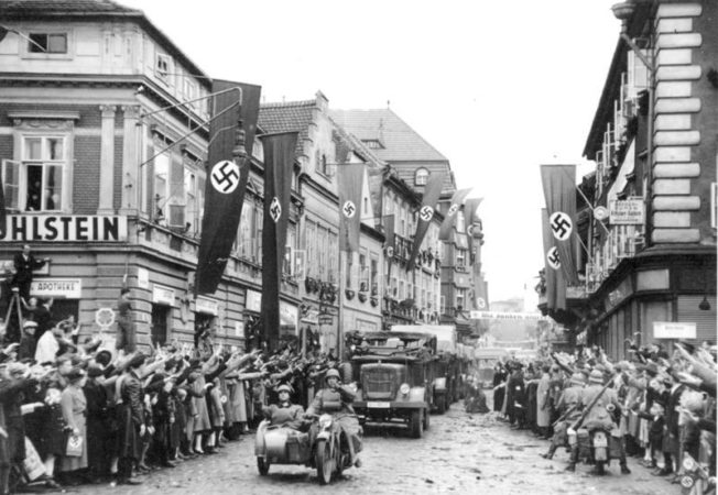Einmarsch in das Sudetenland. Motorisierte deutsche Truppen in Saaz. German mechanized troops enter Saaz. The streets are decorated with swastika flags and banners.
9.10.1938
14.30 Uhr.
Saaz. Sudetenland